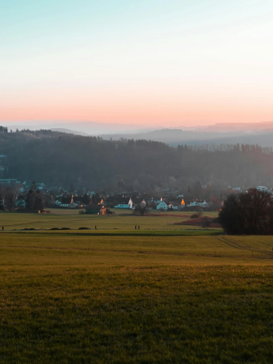 a person flying a kite on top of a lush green field, photo of zurich, eden at dawn, winter setting, quaint village