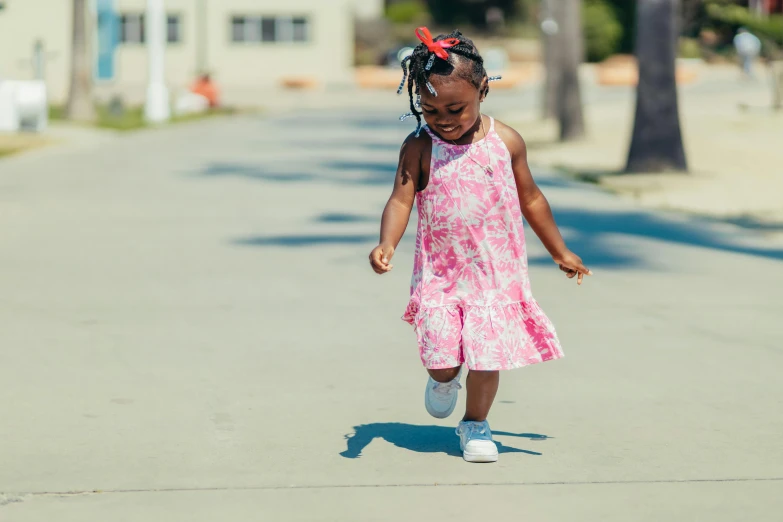 a little girl riding a skateboard down a street, by Stokely Webster, pexels contest winner, wearing an african dress, having fun in the sun, beautiful pink little girl, walking at the park