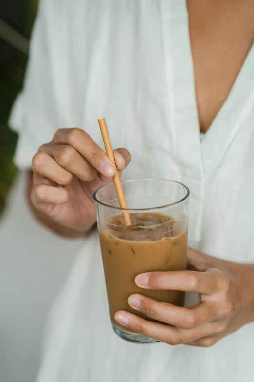 a woman holding a glass of iced coffee, inspired by Ruth Jên, chopsticks, zoomed in, d-cup, light brown