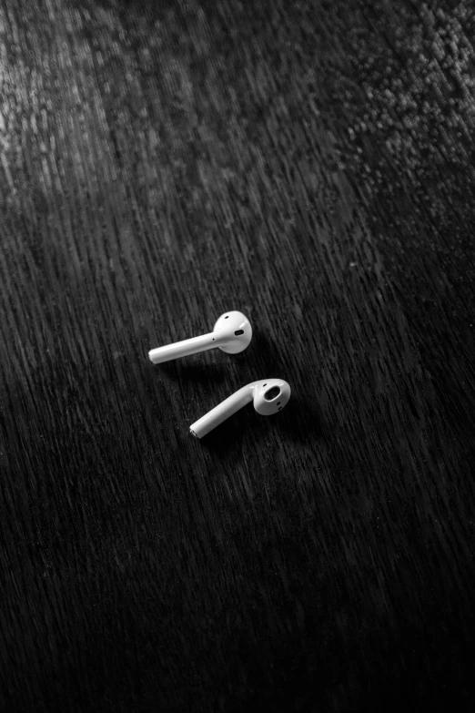 a pair of ear buds sitting on top of a wooden table, inspired by Robert Mapplethorpe, unsplash, monochrome 3 d model, plain background, airpods, nigth