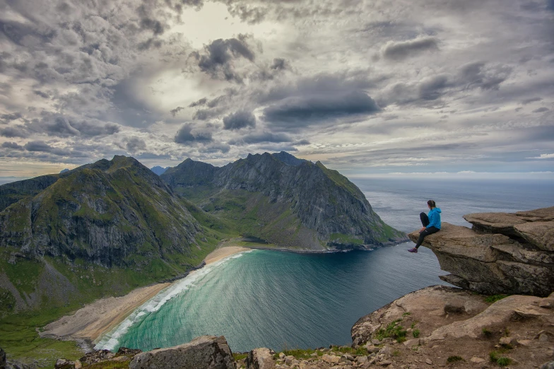 a person sitting on a rock overlooking a body of water, by Roar Kjernstad, pexels contest winner, mountains and ocean, avatar image, gigapixel photo, beach is between the two valleys