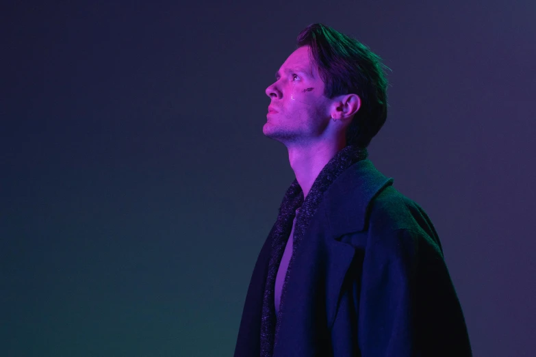 a man standing in front of a purple light, an album cover, inspired by Nikolaj Abraham Abildgaard, looking away from camera, [ theatrical ], wearing black overcoat, profile view