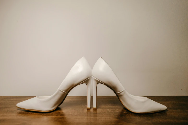 a pair of white shoes sitting on top of a wooden table, heels, white backdrop, multiple stories, unedited