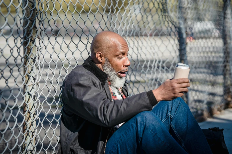 a man sitting on the ground with a cup of coffee, a portrait, inspired by James E. Brewton, pexels contest winner, rusty chain fencing, dave chappelle, mobile, humans of new york