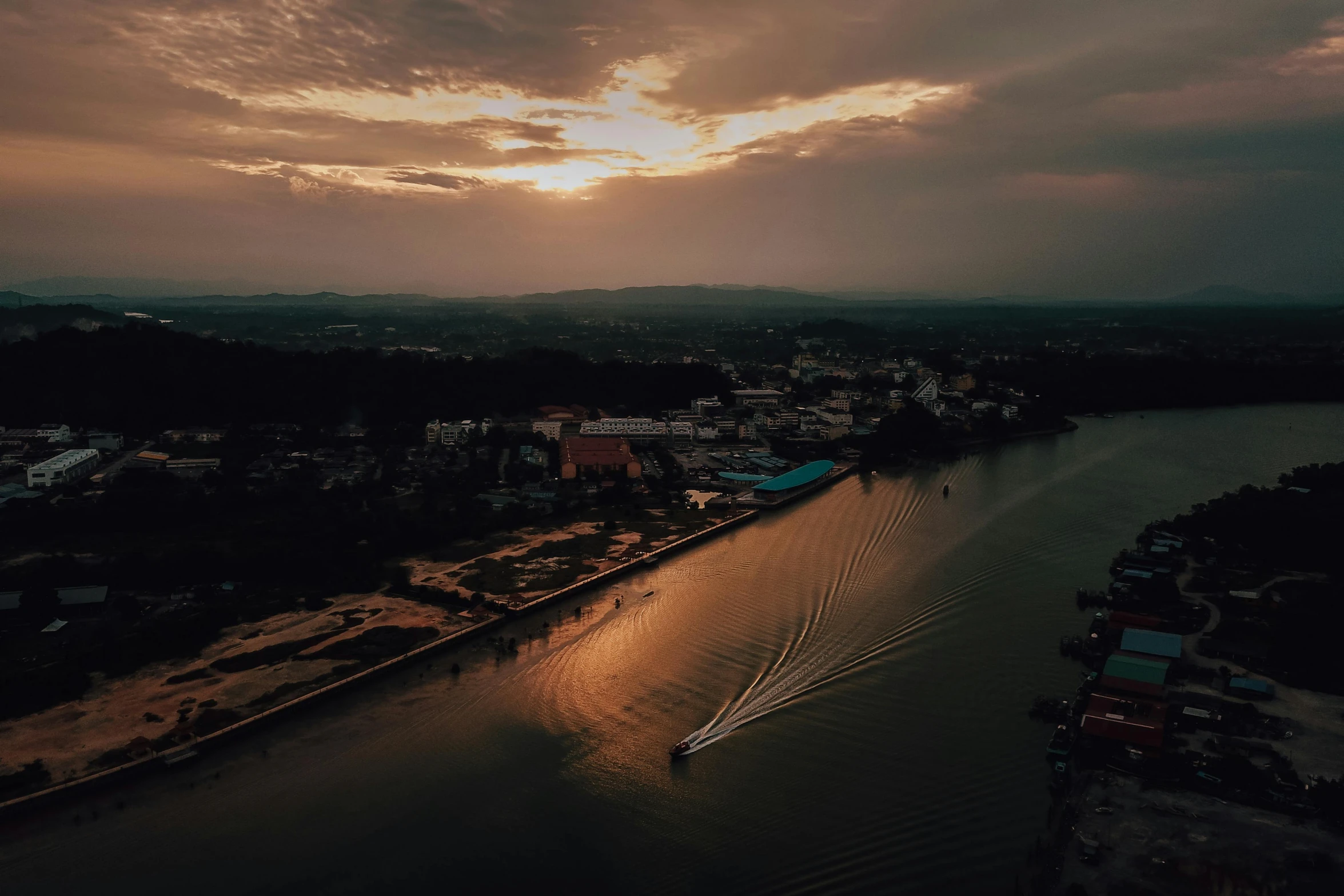 a boat traveling down a river under a cloudy sky, pexels contest winner, dramatic lighting from above, city sunset, laos, low quality footage