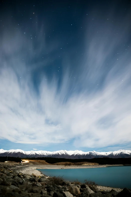 a body of water with mountains in the background, by Peter Churcher, unsplash contest winner, hurufiyya, cirrus clouds, nightsky, te pae, snowy plains