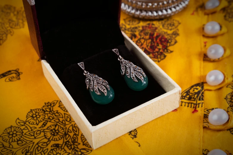 a pair of earrings in a box on a table, pexels contest winner, hurufiyya, ornate dark green clothing, thumbnail, shot on sony a 7, silver ornaments