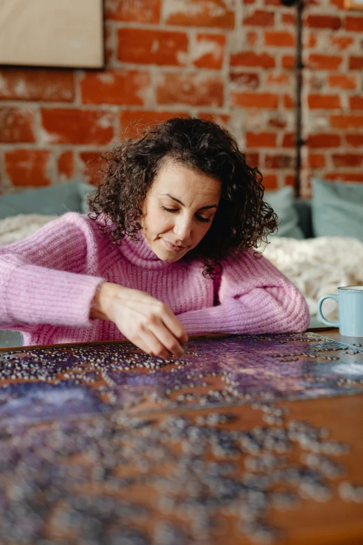 a woman sitting at a table with a puzzle, a jigsaw puzzle, by Julia Pishtar, beans, purple, cosy, having a great time