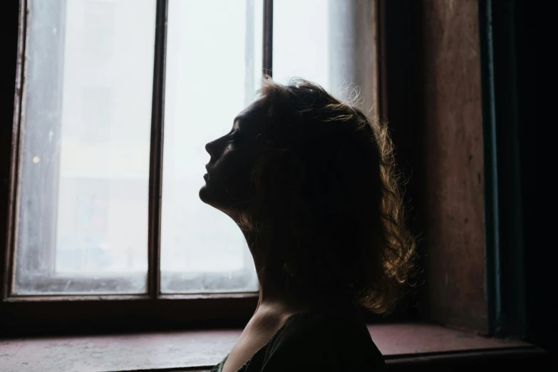 a woman looking out a window in a dark room, inspired by Elsa Bleda, pexels contest winner, renaissance, perfect crisp sunlight, profile image, young woman looking up, outlined silhouettes