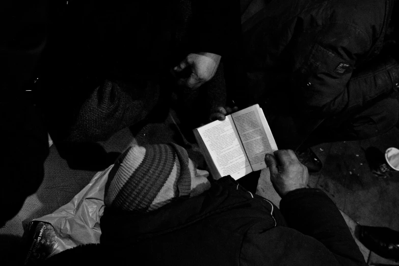 a black and white photo of a person reading a book, a black and white photo, by Matija Jama, cyberpunk homeless, worshipers, cold freezing nights, photo on iphone