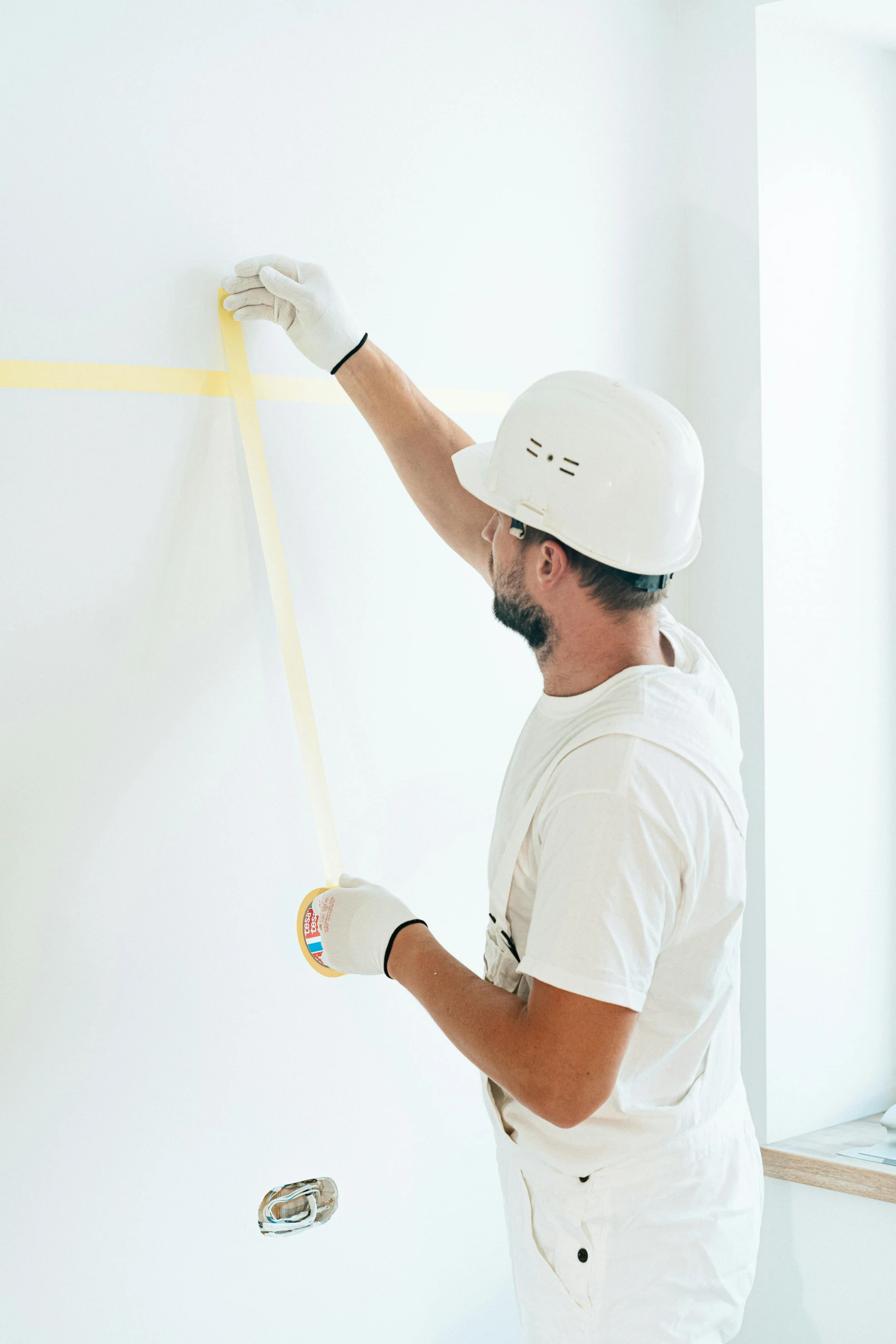 a man is painting a wall with yellow tape, by Francis Helps, pexels contest winner, hard hat, plain background, measurements, instagram story