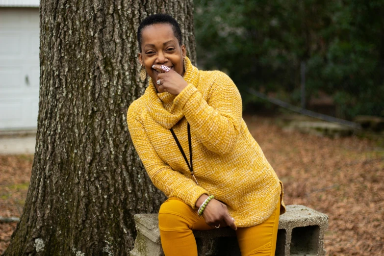 a woman sitting on a bench next to a tree, a portrait, by Bradley Walker Tomlin, pexels contest winner, black and yellow tracksuit, satisfied pose, african american woman, wearing an oversized sweater