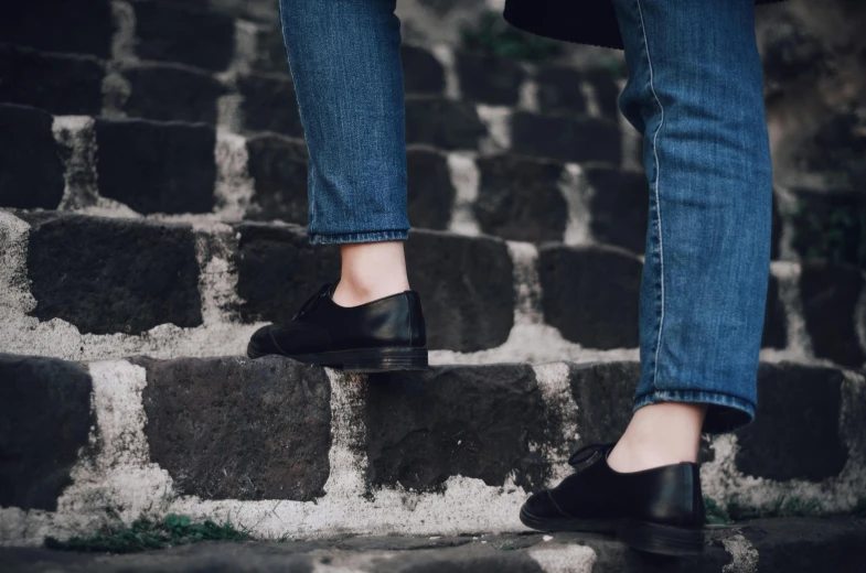 a person standing on some steps wearing black shoes, pexels contest winner, wearing jeans, background image, female ascending, stone steps