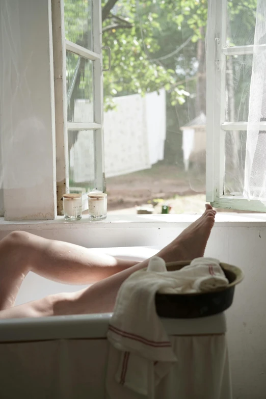 a woman laying in a bathtub next to a window, inspired by Andrew Wyeth, unsplash, al fresco, barefeet, pale, summer feeling