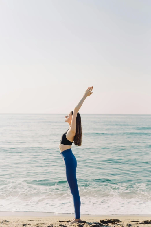 a woman standing on top of a beach next to the ocean, arabesque, raised hand, profile image, stretch, clean face and body skin