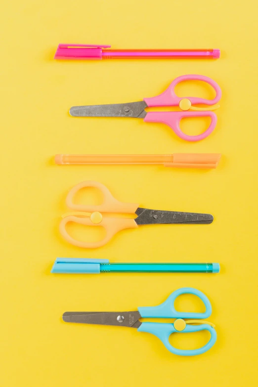 a group of scissors sitting next to each other on a yellow surface, jen atkin, educational supplies, fluorescent, holding pencil