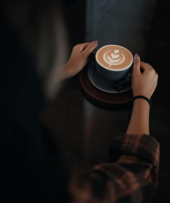 a person sitting at a table with a cup of coffee, wearing a dark sweater, top selection on unsplash, latte art, promo image