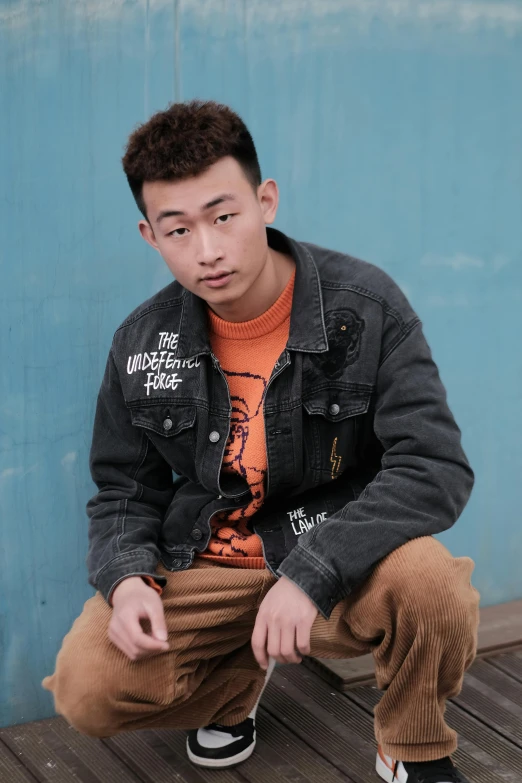 a man sitting on top of a wooden floor next to a blue wall, an album cover, inspired by Huang Gongwang, trending on pexels, wearing a jeans jackets, headshot profile picture, wearing punk clothing, ismail inceoglu and ruan jia