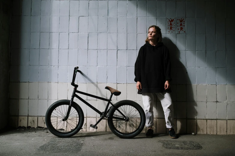 a man standing next to a bike leaning against a wall, inspired by Seb McKinnon, press shot, stealthy, profile image, casey cooke