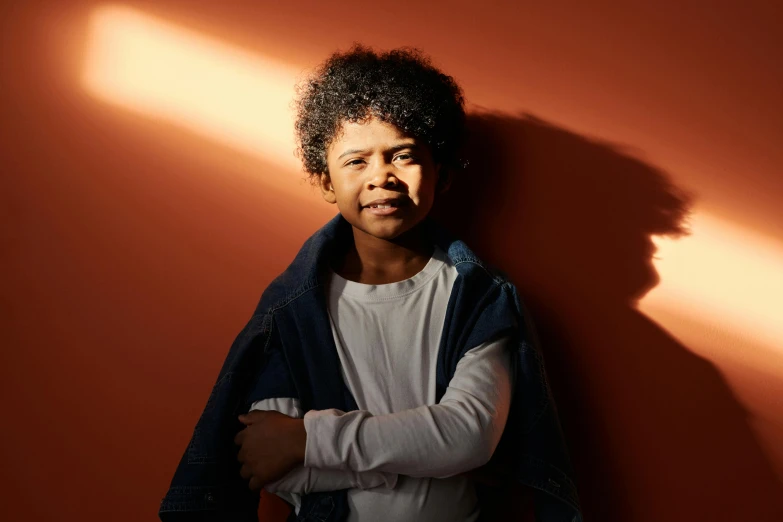 a man leaning against a wall with his arms crossed, an album cover, by Niels Lergaard, pexels contest winner, light skinned african young girl, in a sunbeam, little boy, studio backlight