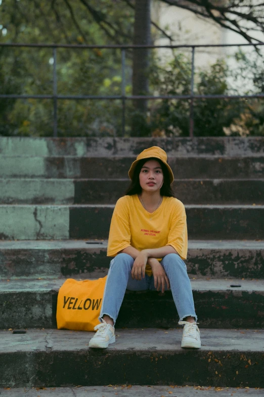 a woman sitting on some steps with a yellow bag, unsplash contest winner, wearing a t-shirt, ulzzang, yellow cap, 2019 trending photo