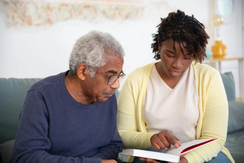 a woman sitting on a couch next to a man who is reading a book, a photo, african american, nursing home, profile image, colour corrected