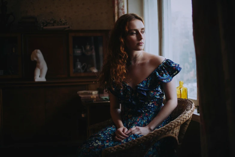 a woman sitting in a chair looking out a window, a portrait, inspired by Elsa Bleda, pexels contest winner, renaissance, sullen old maid ( redhead, a blue dress, patterned clothing, medium format. soft light