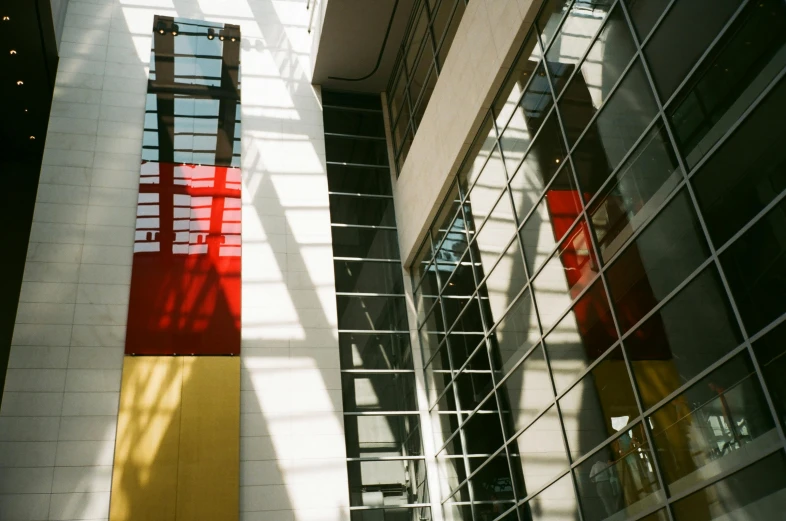 a red sign hanging from the side of a tall building, a photo, bauhaus, light through glass, yellow and red color scheme, atrium, calarts