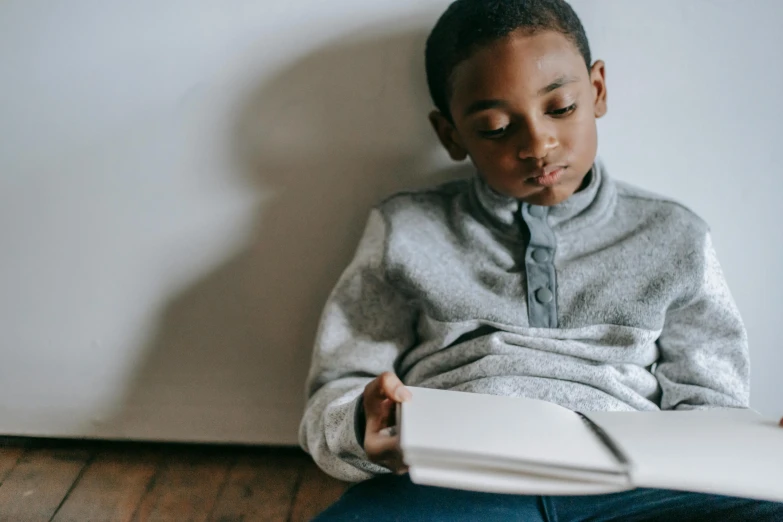 a young boy sitting on the floor reading a book, by Matija Jama, pexels contest winner, black teenage boy, gif, boy with neutral face, informative texts