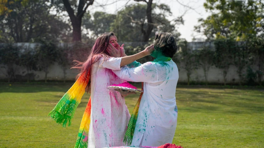 a couple of people standing on top of a lush green field, a colorized photo, by Riza Abbasi, pexels contest winner, action painting, her face is coated in a white, festive colors, bleeding colors, performance