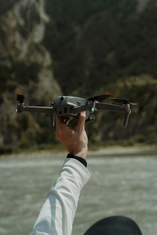 a person holding a remote control device over a body of water, drone footage, cinematic shot ar 9:16 -n 6 -g, low quality photo, movie filmstill