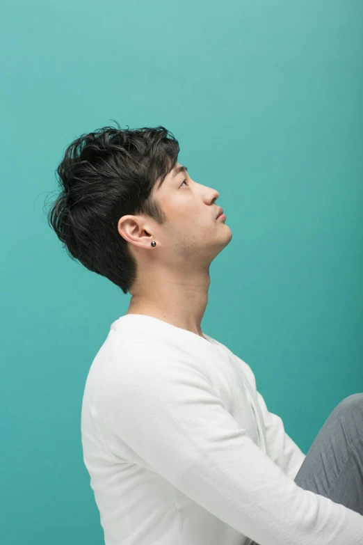 a man sitting on the floor in front of a blue wall, an album cover, inspired by Joong Keun Lee, trending on pexels, strong jawline, profile view, ayami koj ima, androgynous person