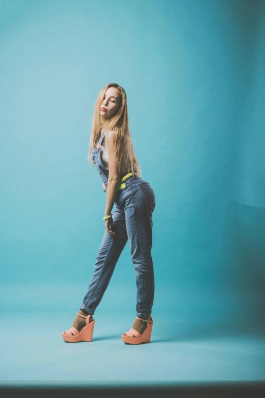 a woman standing in front of a blue background, tight blue jeans and cool shoes, 5 0 0 px models, trending on imagestation, yellow overall