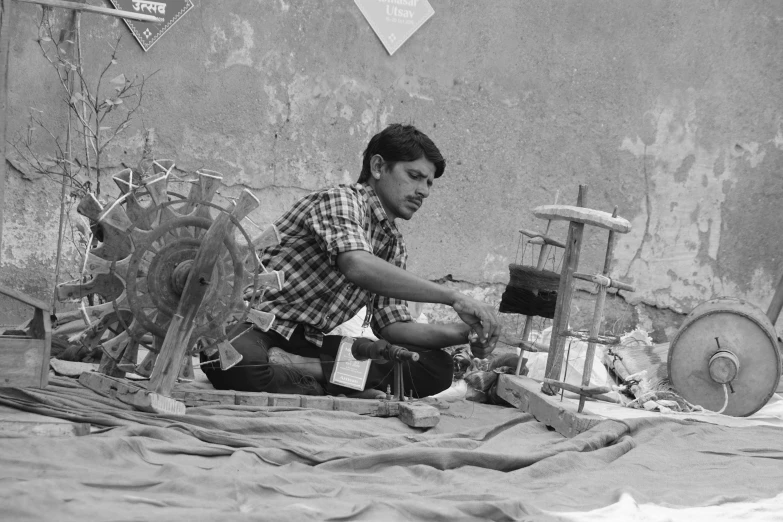 a black and white photo of a man sitting on the ground, a silk screen, by Sunil Das, flickr, intricate machinery, spinning, people at work, a photo of a man