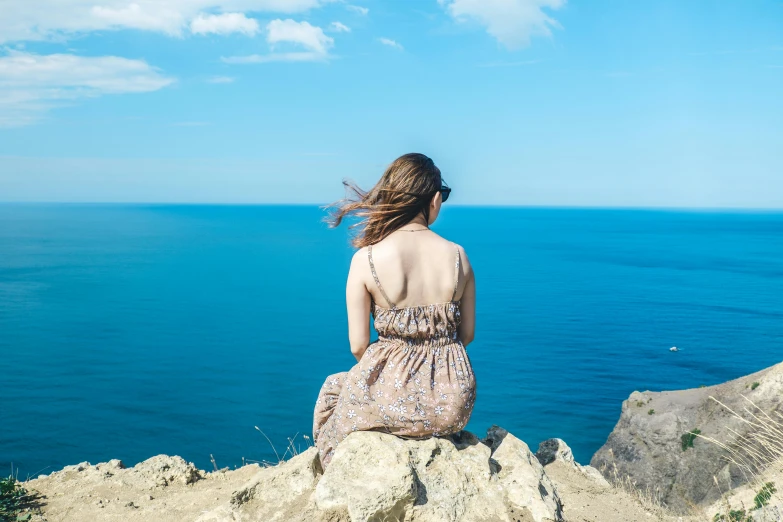 a woman sitting on a rock overlooking the ocean, pexels contest winner, romanticism, wearing a sundress, cliffs of dover, blue sky, profile image