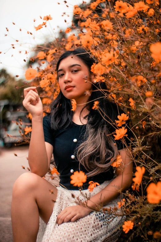 a woman sitting in front of a bush with orange flowers, trending on pexels, beautiful asian girl, style of ade santora, various posed, autum