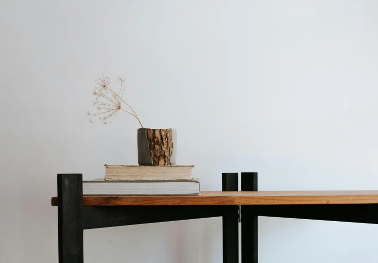 a stack of books sitting on top of a wooden table, a minimalist painting, unsplash, ikebana, teak table, made of wrought iron, gallery display photograph