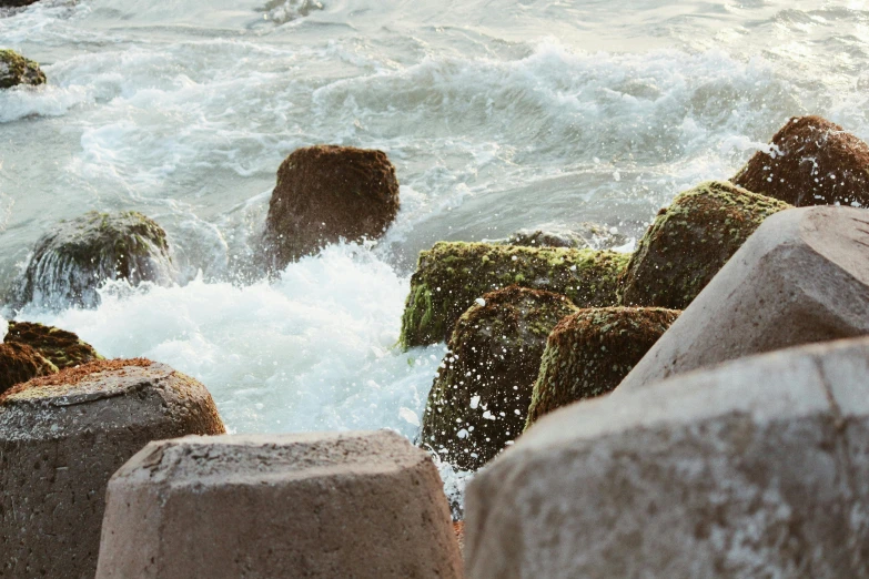 a man riding a surfboard on top of a wave, a picture, unsplash, happening, moist mossy white stones, ((rocks)), jagged blocks of stone, near a jetty