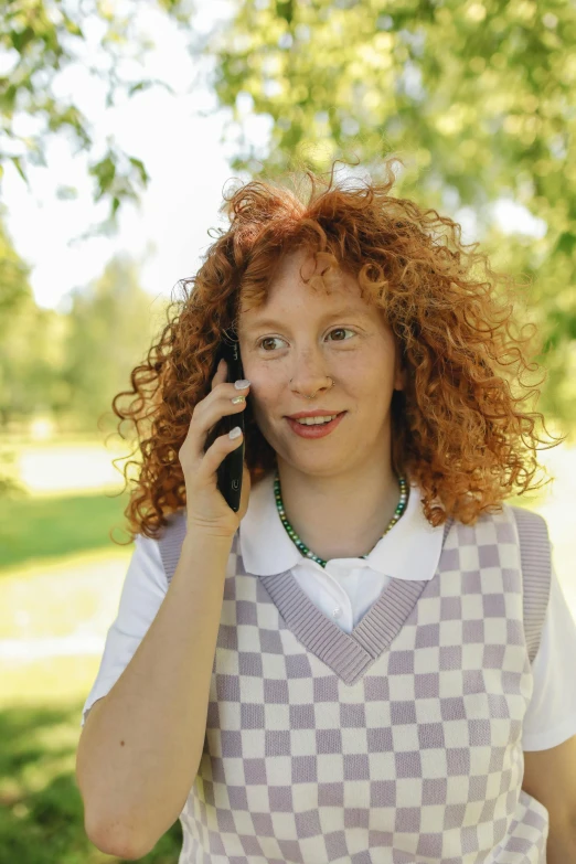 a woman with red hair talking on a cell phone, wearing a school uniform, with a curly perm, a park, 2019 trending photo