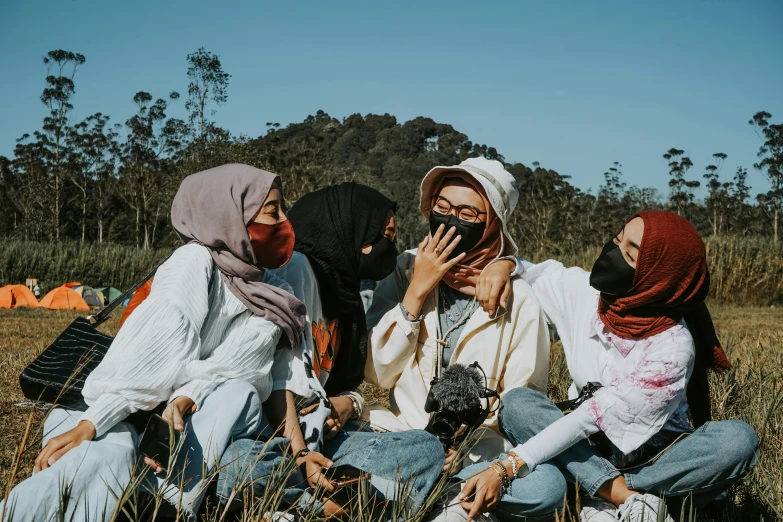 a group of women sitting on top of a grass covered field, trending on pexels, hurufiyya, balaclava covering face, malaysian, wearing a fisher 🧥, bandana