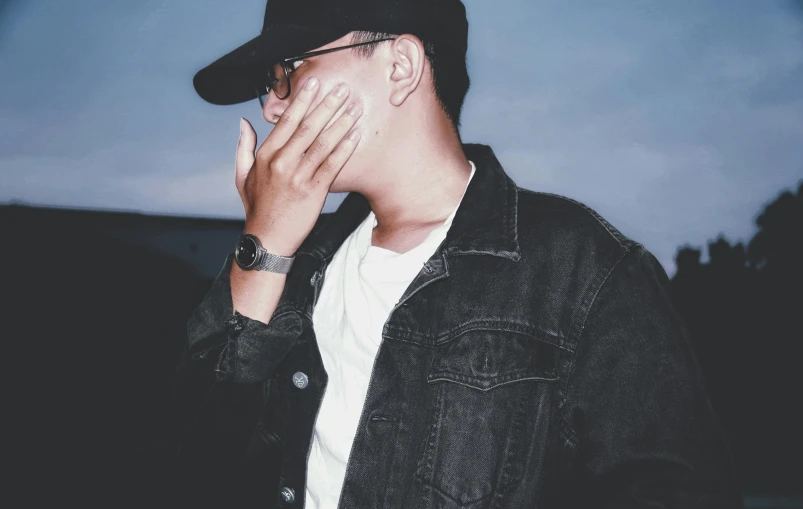 a man holding his hand to his face, an album cover, inspired by Gang Hui-an, trending on pexels, realism, ☁🌪🌙👩🏾, wearing black glasses, hand holding cap brim, night photo