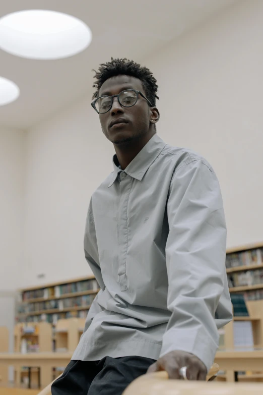 a man sitting on a bench in a library, an album cover, inspired by Xanthus Russell Smith, trending on unsplash, grey skinned, standing in class, serious look, glassy