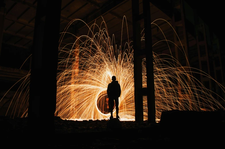 a person standing in front of a fire, by Sebastian Spreng, pexels contest winner, visual art, large electrical gold sparks, steel mill, silhouette of a man, vsco film grain