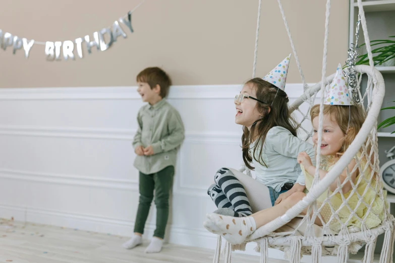 a couple of kids that are sitting in a hammock, by Emma Andijewska, pexels contest winner, at a birthday party, decoration around the room, 15081959 21121991 01012000 4k, wearing a light grey crown