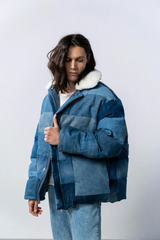 a man standing in front of a white wall wearing a blue jacket and jeans, an album cover, inspired by Sadao Watanabe, unsplash, model wears a puffer jacket, patchwork, thumbnail, flannel