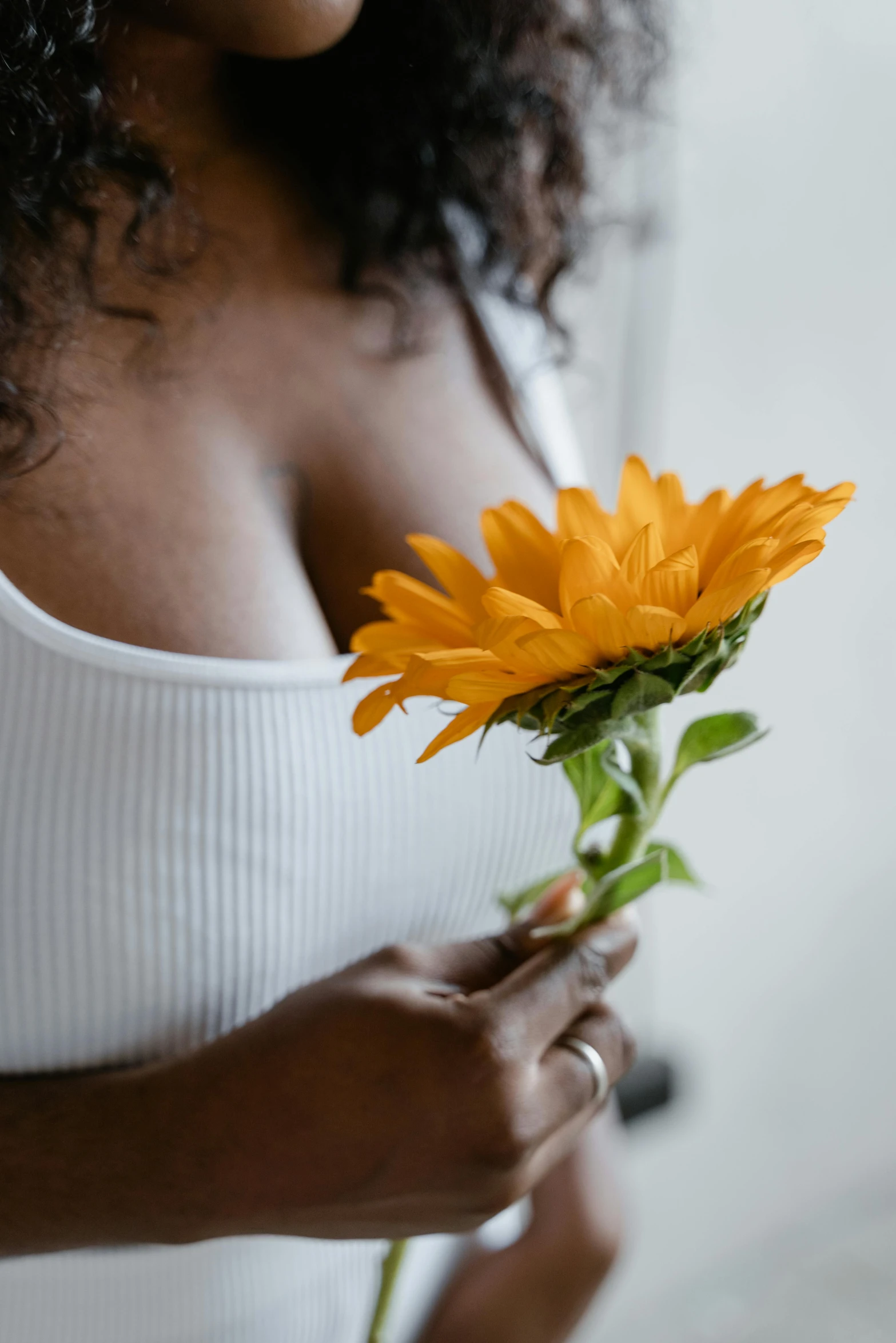 a close up of a person holding a flower, by Everett Warner, trending on unsplash, renaissance, white bra, marigold, wearing a low cut tanktop, black young woman