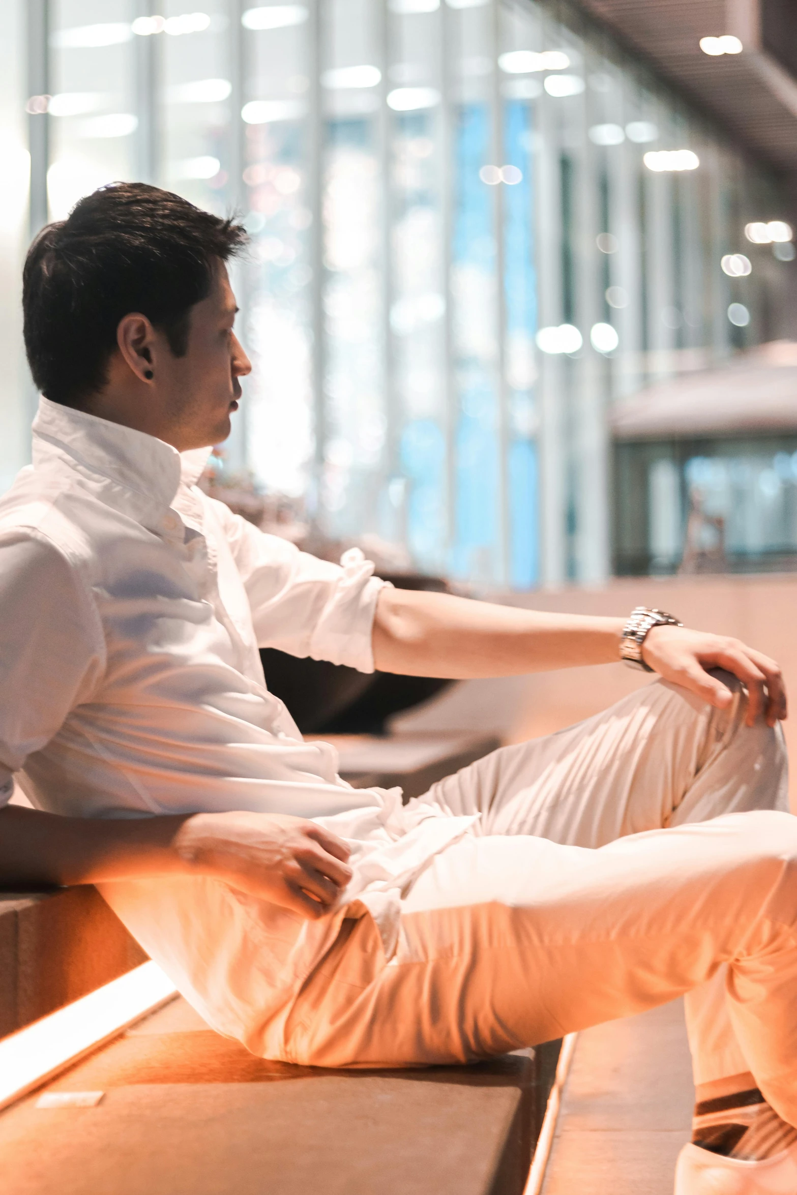 a man sitting on a bench in an airport, inspired by Raymond Han, happening, wearing white shirt, elegant profile pose, jakarta, **cinematic