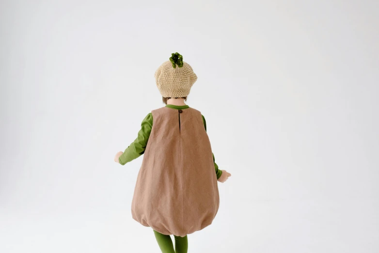 a close up of a doll on a white surface, an album cover, inspired by Elsa Beskow, shin hanga, green and brown clothes, back view. nuri iyem, an avocado chair, an oversized beret