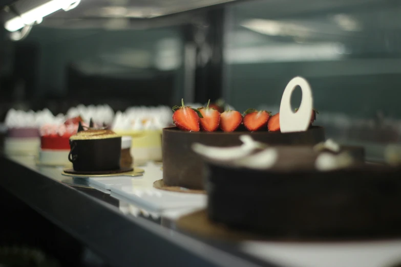 a row of cakes sitting on top of a counter, lachlan bailey, chocolate city, next to sliced strawberries, hot food