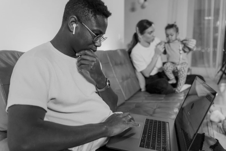 a man sitting on a couch using a laptop computer, a black and white photo, by Carey Morris, pexels, portrait of family of three, mkbhd, lawther sit at table playing dnd, 🤬 🤮 💕 🎀